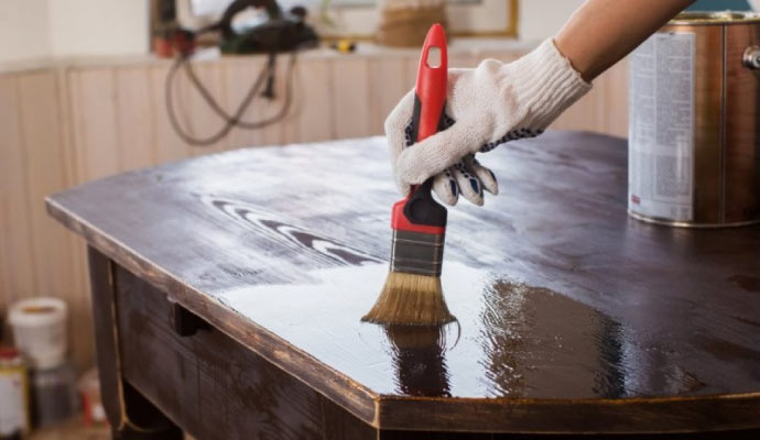 A person varnishing a wooden table using equipment