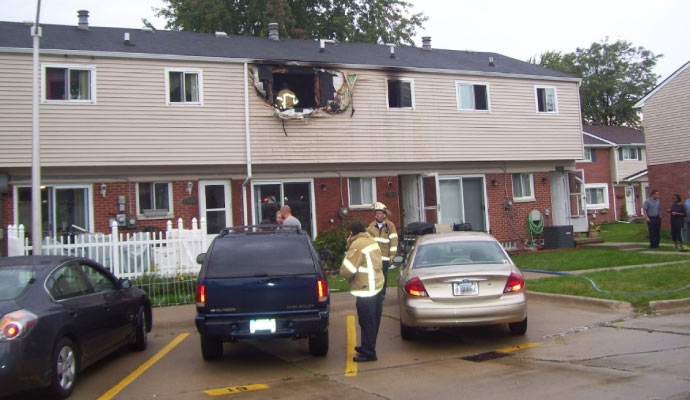 firefighters inspecting fire damage to a second-floor apartment in a residential building