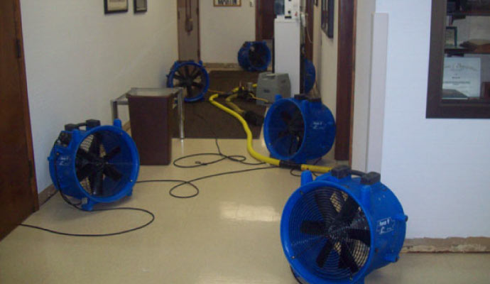 multiple blue industrial fans and dehumidifiers set up in a hallway for water damage restoration