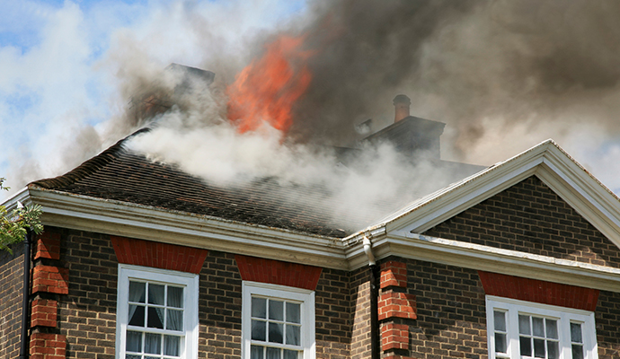 Fire damaged house with dark smoke billowing from the roof Fire damaged house with dark smoke billowing from the roof