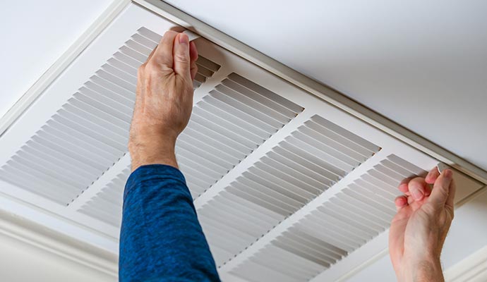 Person removing or adjusting air vent from ceiling Person removing or adjusting a white air vent from a white ceiling for maintenance or cleaning