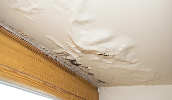 Ceiling damage caused by roof leak Ceiling with water damage showing bubbling paint and discolored areas caused by a roof leak