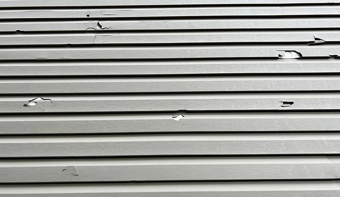Hail-damaged vinyl siding with visible cracks Hail-damaged vinyl siding with visible cracks