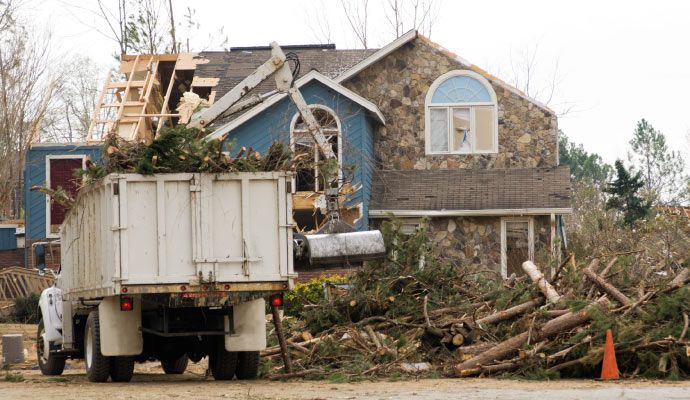 Storm damage house cleanup and debris removal by truck Cleanup truck clearing storm debris from disaster-damaged property